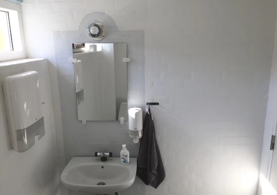 Foto af et rent og lyst badeværelse med hvidt toilet, hvidt spejl, håndklæde og håndsæbe i hvidt håndskærm.