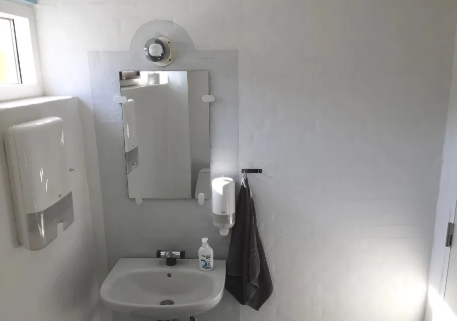 Foto af et rent og lyst badeværelse med hvidt toilet, hvidt spejl, håndklæde og håndsæbe i hvidt håndskærm.