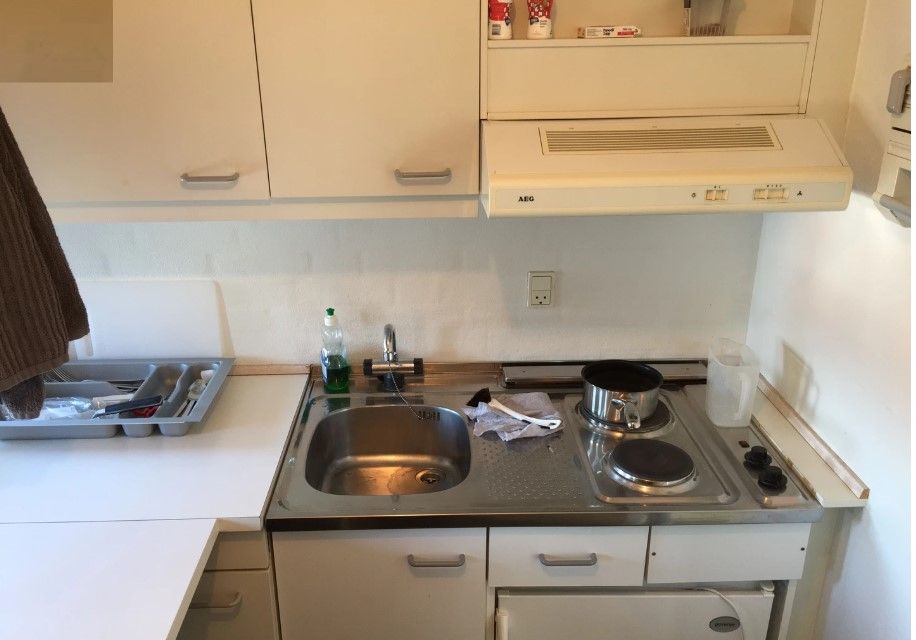 Lyst køkken med lyse højskabe, AEG ovn, AEG komfur, vaskebækken og en stor metalskuffe