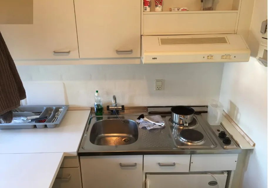 Lyst køkken med lyse højskabe, AEG ovn, AEG komfur, vaskebækken og en stor metalskuffe