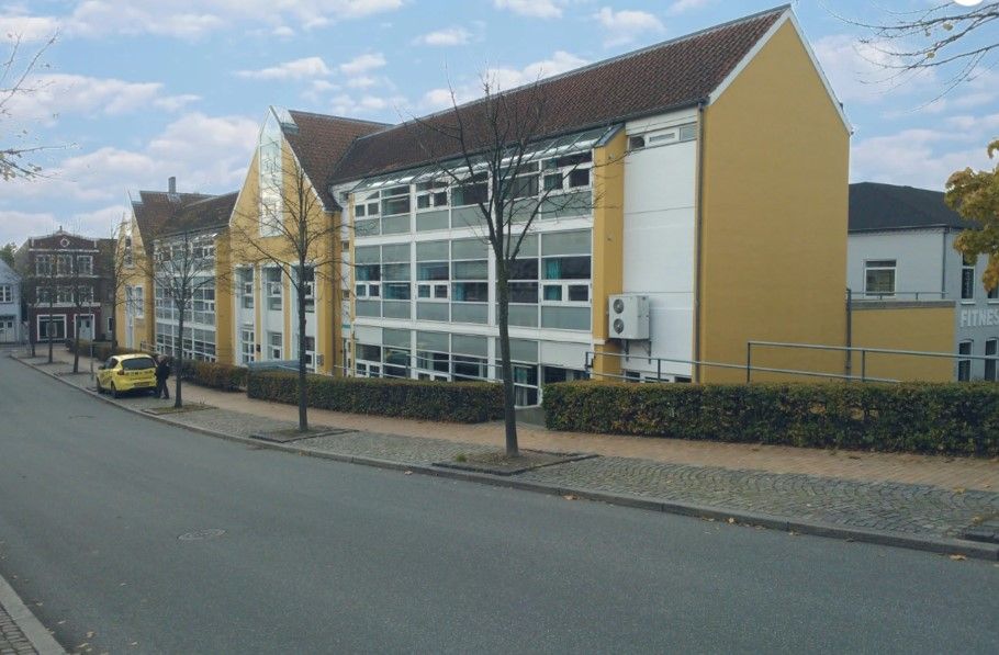 To høje bygninger med gul facade og vinduer, et fitnesscenter og en parkeringsplads med en parkeret gul bil