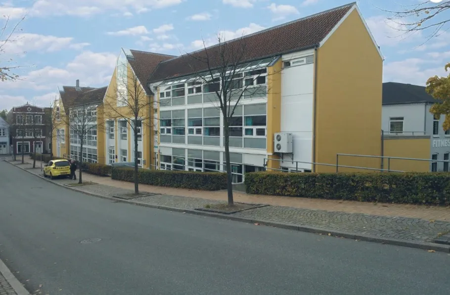 To høje bygninger med gul facade og vinduer, et fitnesscenter og en parkeringsplads med en parkeret gul bil