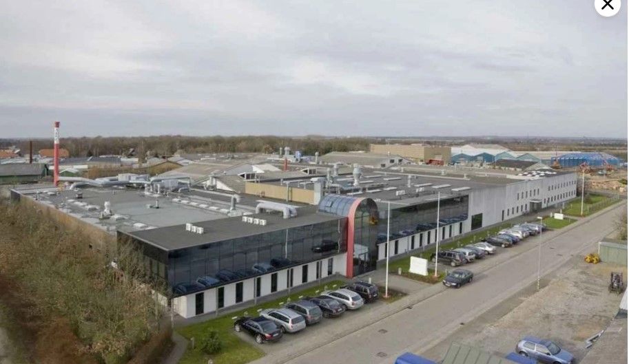 Store fabriksbygning med glasvinduet og mange parkerede biler foran bygningen