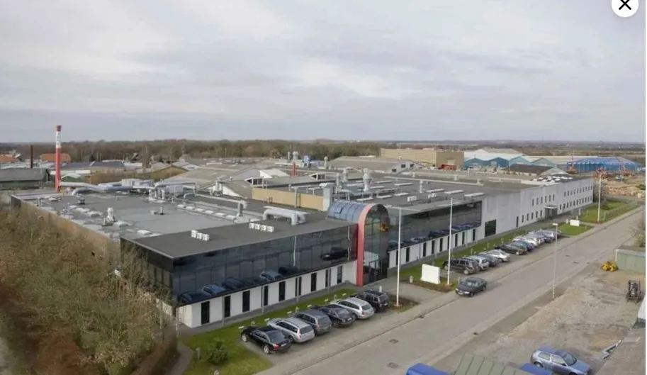 Store fabriksbygning med glasvinduet og mange parkerede biler foran bygningen