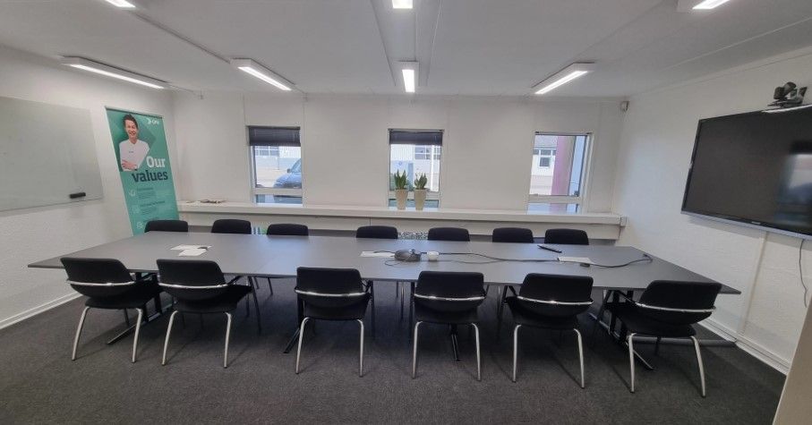 Store mødelokale med skrivebord, stole, whiteboard, projektor og plantepoter på vindueskarmen.