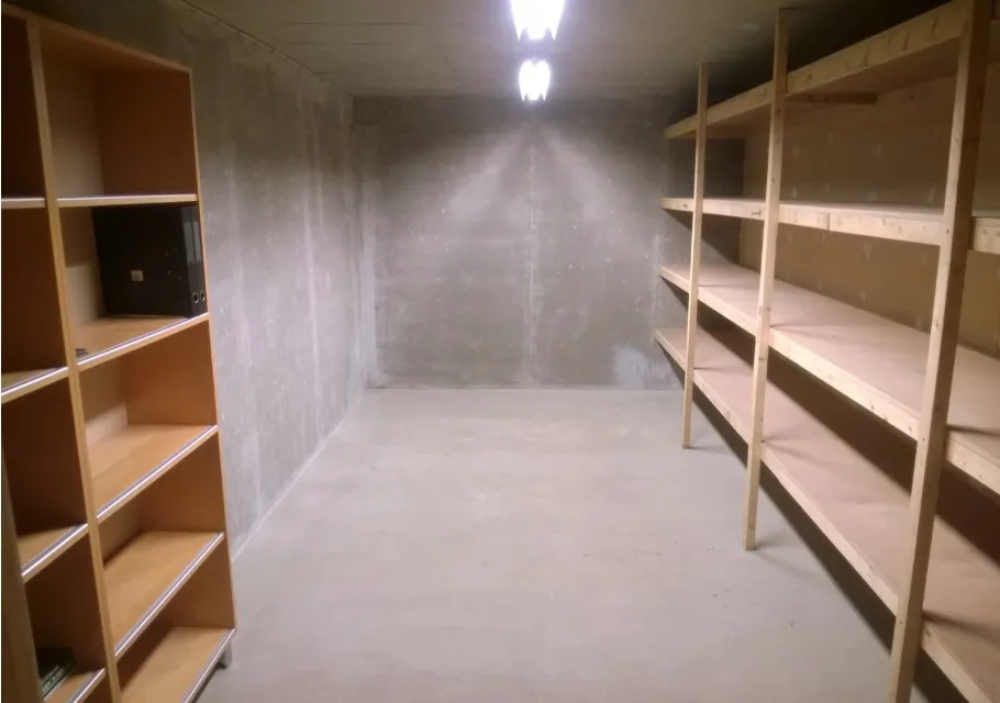 Ledig kælderrum med to træhylder og møbler til opbevaring. Rummet er tørt og har lys og betonvægge.