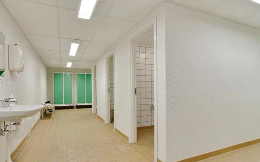 En tom gang med toiletrum og badeværelser med hvidt og grønt. Der er håndvask og håndklædeholder.