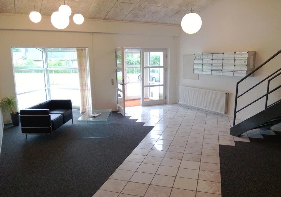 Kontor med glasdøre og glasbord med to sofaer, hvor der er en plante i en potte og en hvid radiator på væggen