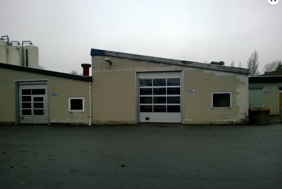 Lejlighed med stor garagedør og to små ruder. En plante i en stor gryde står på hjørnet af bygningen.