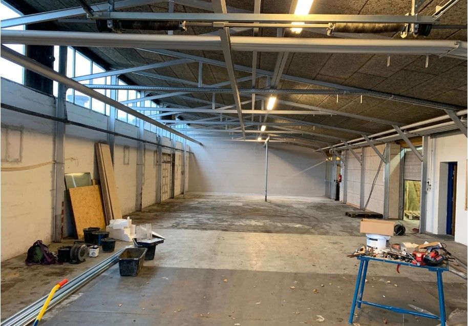 En stor, tom industrihal med lysegul væg og metalliske loftsbjælker samt gul bord med værktøj og rulle med