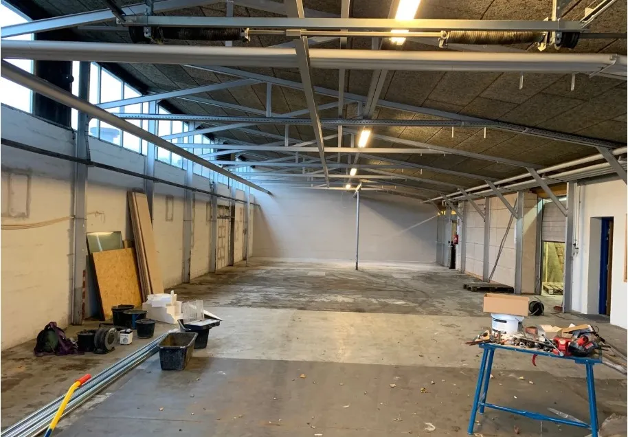 En stor, tom industrihal med lysegul væg og metalliske loftsbjælker samt gul bord med værktøj og rulle med