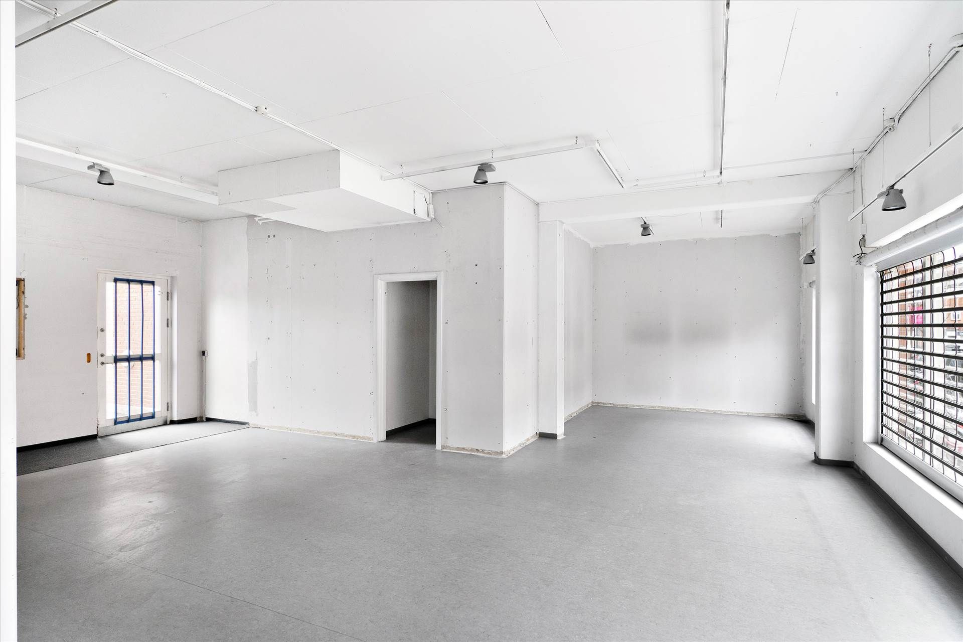 En stor, hvid, ubenyttet lejemål med lyse lofter og vægge samt to indgange og en stor vindue.