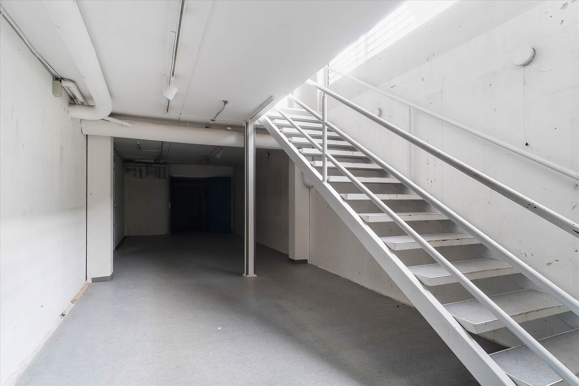 Styretræk, hvidt gulv og lyse loft, som fører op til en lys indgangsdør.