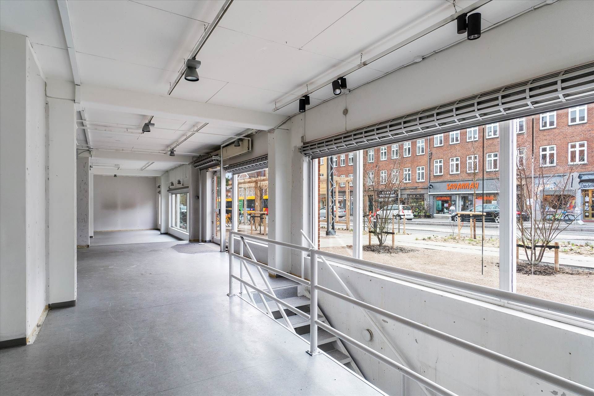 Moderne og lyse lokaler med store ruder og højloft, lysekroner, vinduesruder og trappe med hvidt metalgevær.