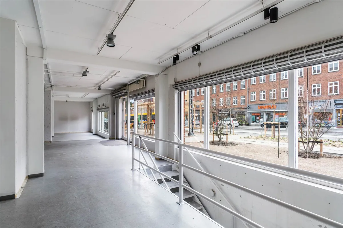 Moderne og lyse lokaler med store ruder og højloft, lysekroner, vinduesruder og trappe med hvidt metalgevær.