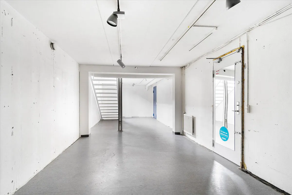 Lejlighedshus med hvide vægge og gulve, en dør og en stige inde i bygningen samt flere lysekroner og et kamera på loftet