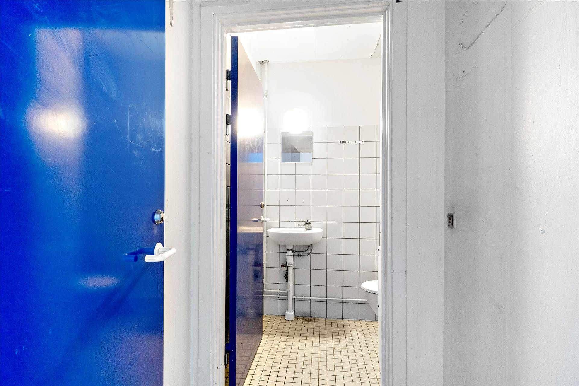 Lejlighed med moderne toilet, hvidt keramikbadekar, hvidt badebord og en blå dør med hvid håndtag i en hvid og blå