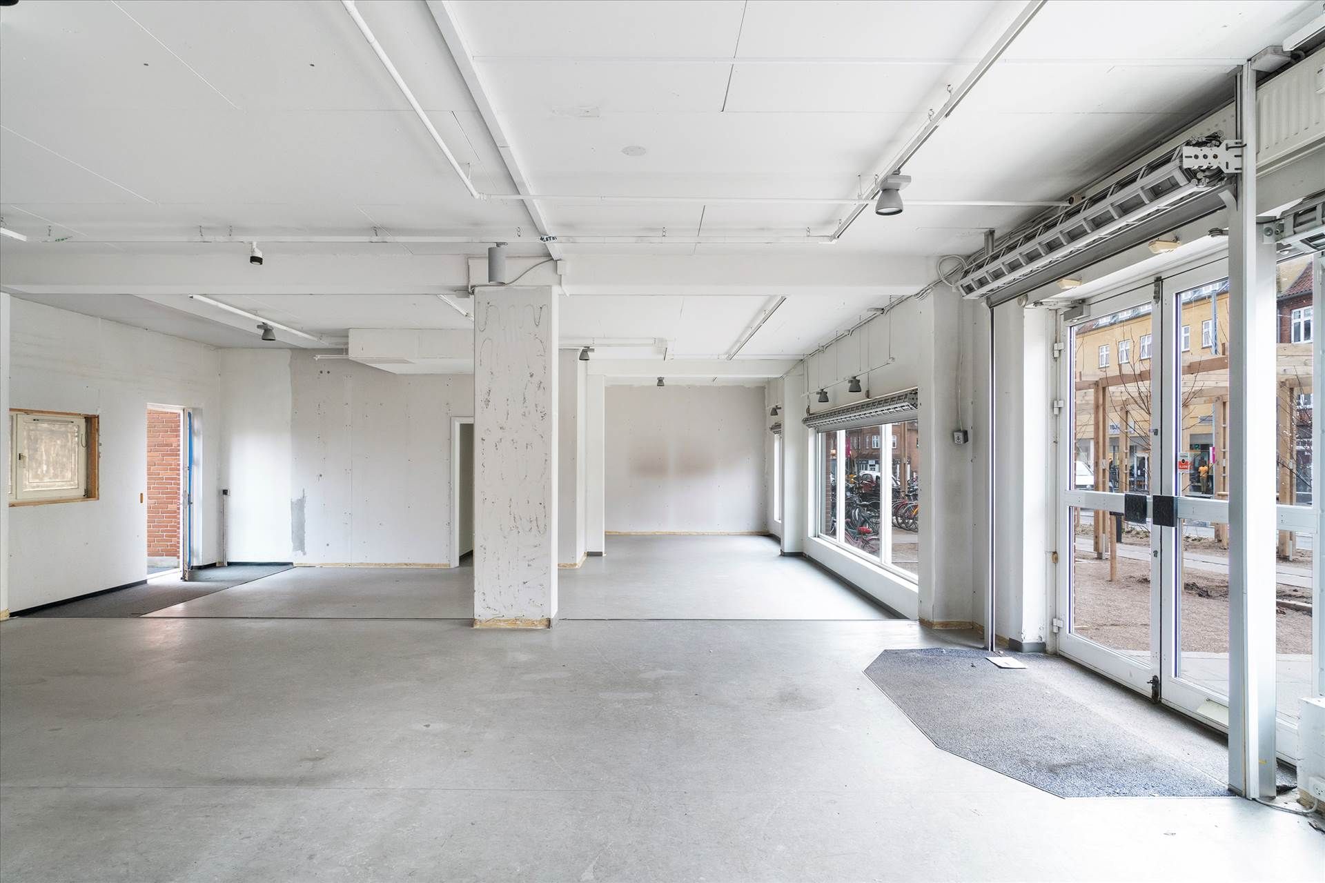 Hjørne lokale i Søborg med store vinduer og glasdøre mod gaden og højt loft. Lokalerne er uden møbler og har en simpel