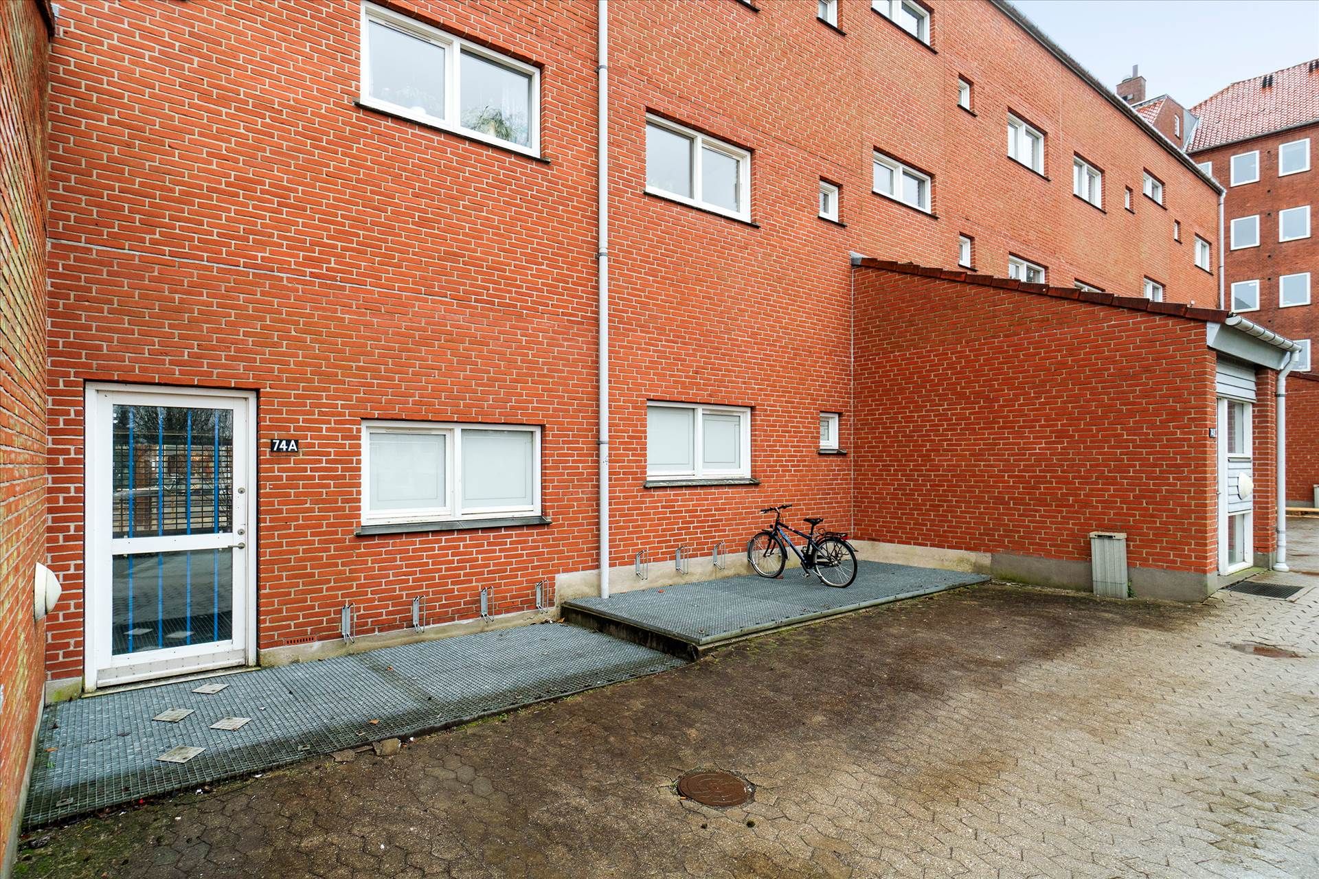 Lejlighed med kælder og cykelstativ, der er parkeret foran rødmalet bygning med hvide vindueskarme og nummer 74A på døren