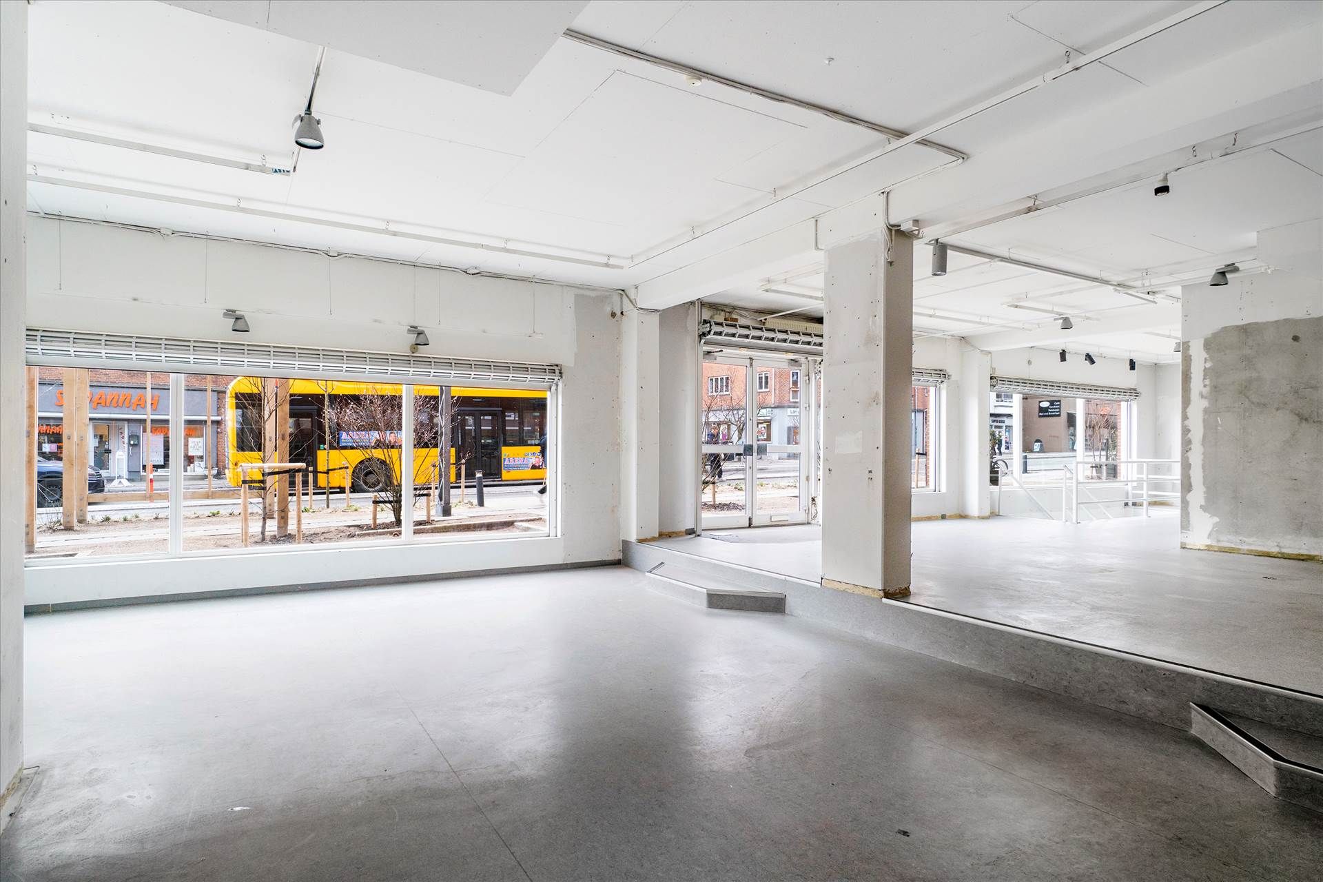 Indvendigt rum med højt loft og store ruder, hvor en bus venter udenfor, og der er en rampe og trin.