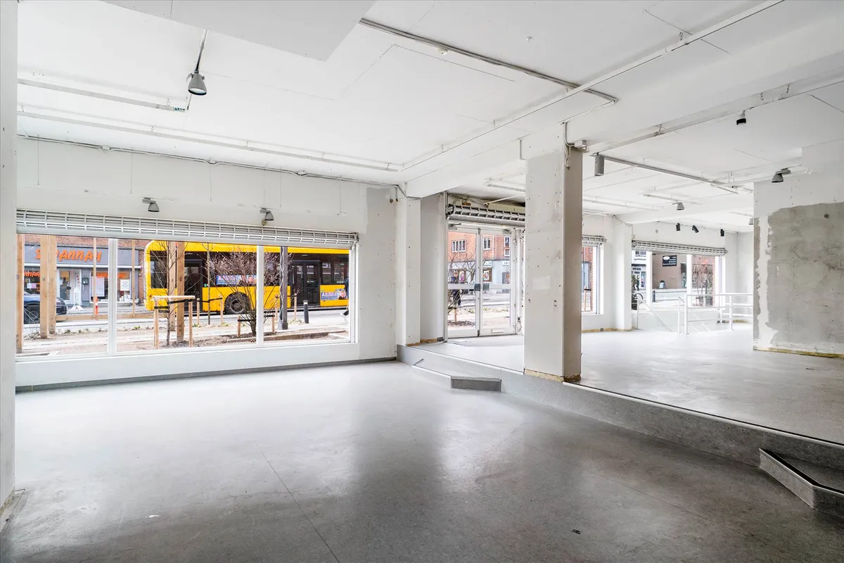 Indvendigt rum med højt loft og store ruder, hvor en bus venter udenfor, og der er en rampe og trin.