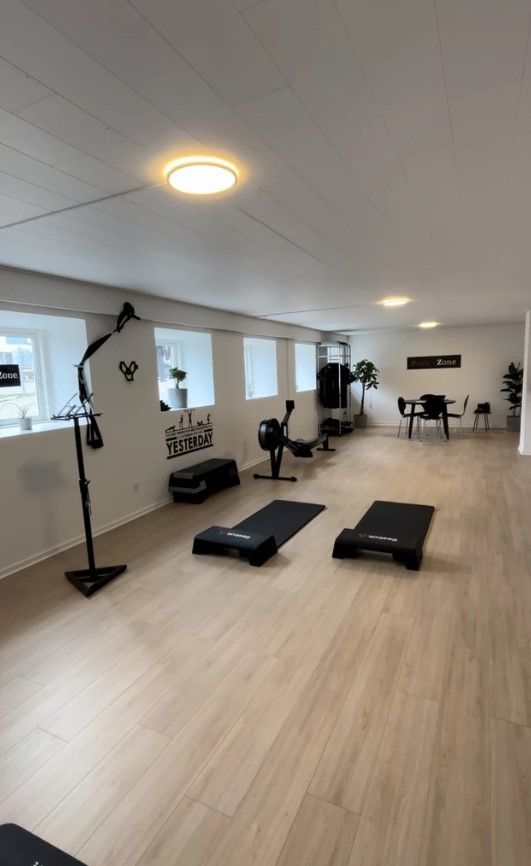 Et tomt lokale med trægulv og hvide vægge, hvor der er træningsudstyr og møbler. Der er skrift på væggen og et gult lys på