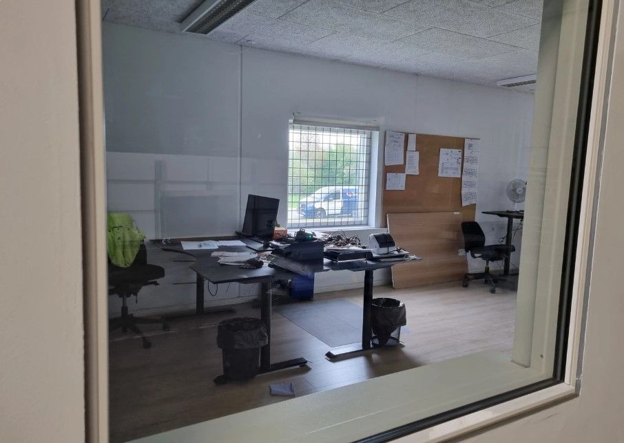 Et moderne kontor med to bord, computere og møbler samt glasruder og et rekvisit i baggrunden