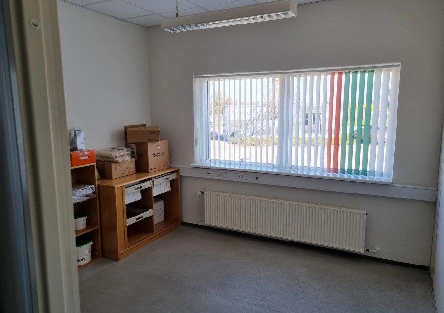 Kontorrum med lyse loftslampe, vindue, radiator og to træhylder med flere papkasser og papirkurve