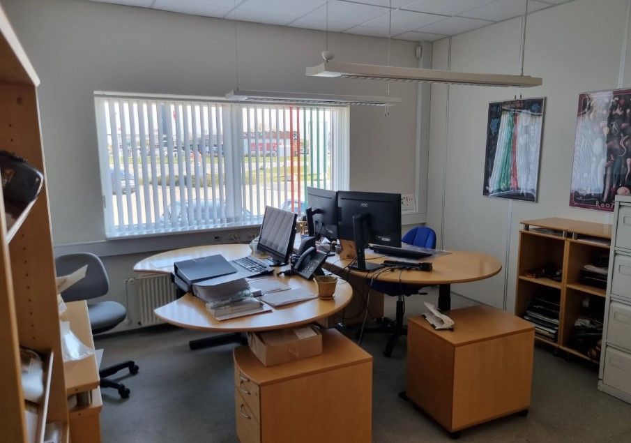 Kontorlokale med to borde, hver med computere og telefoner, to stole og to skriveborde samt et køleskab og et kabinet