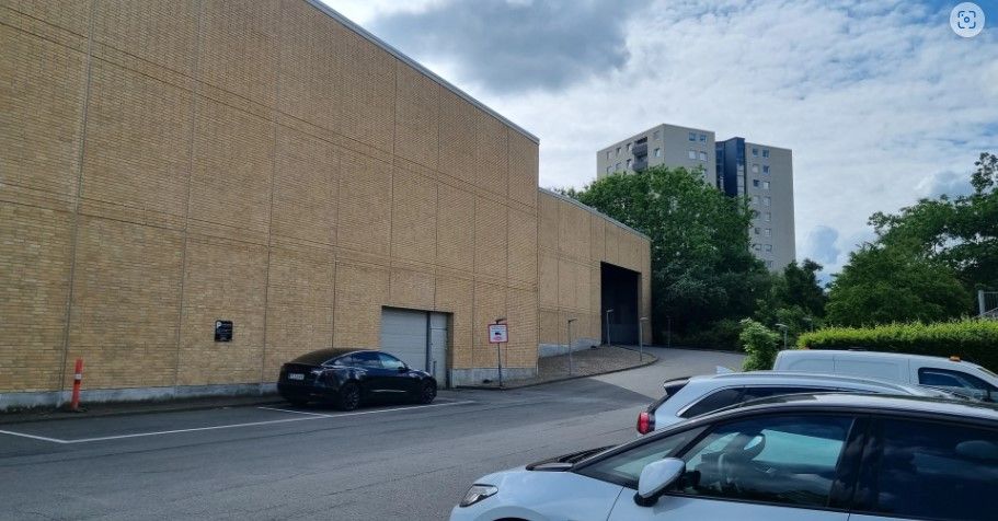 Flere biler parkeret udenfor bygning med garageindkørsler og højre dreje. På afstanden ses bygninger med flere etager og