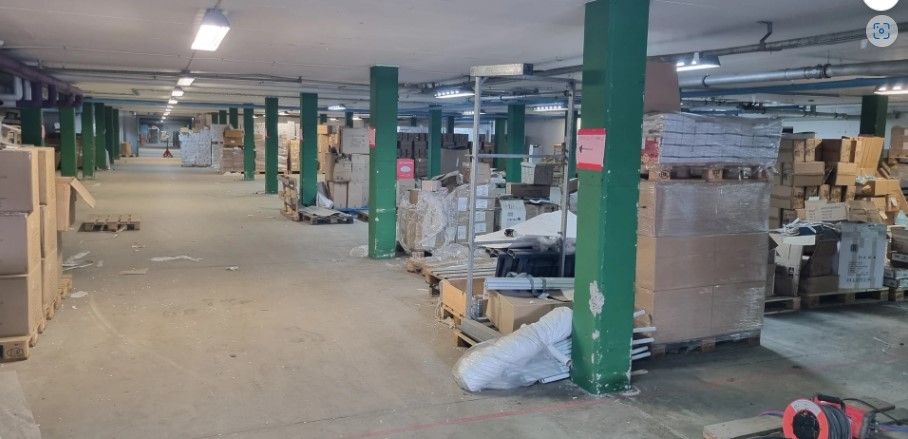 En stor lagerhal med mange kasser og palle og en rød schildet med tekst på.