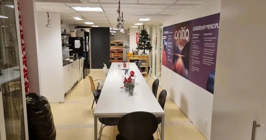 Kontorlokale med langt bord og stole i Ballerup. Væg med plakat, julestjerne og juletræ i køkken.