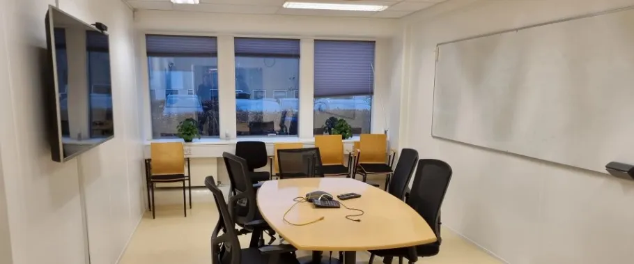 Et moderne kontor med lysegul gulvbelægning, tre vinduer med gardiner, en stor skrivebord og flere stole samt en tv-skærm og