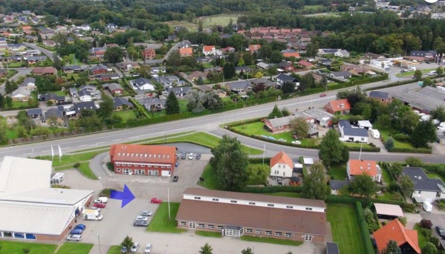 Luftfoto af bygningskomleks i landsbyen med flere boligområder, parker og vejforløb med biler og en busstoppested
