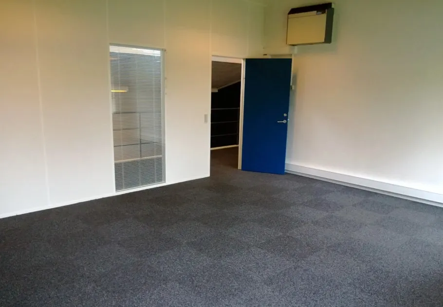 En stor, tom kontorrum med hvide vægge og gulv. En lyseblå dør med håndtag og en hvid dør med vinduesruder. En hvid