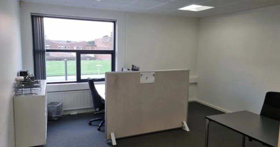 Et stort og rummeligt kontorlokale med højt til loftet, en stor vinduesfront, et højt og bredt skrivebord samt en kontorblok