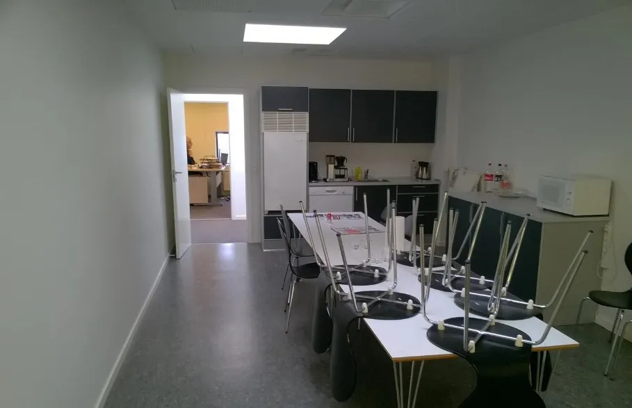 Et tomt kontor med bord og stole samt køleskab og mikrobølgeovn i baggrunden