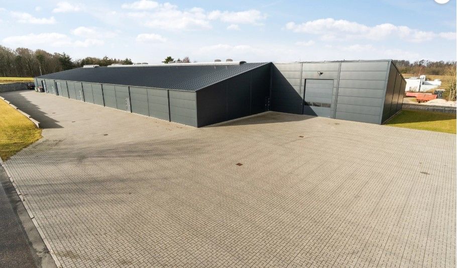 En stor, grå industribygnign med flere garageporte og en stor parkeringsplads foran