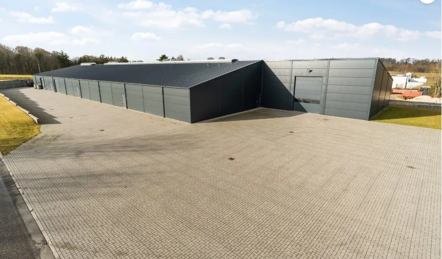 En stor, grå industribygnign med flere garageporte og en stor parkeringsplads foran