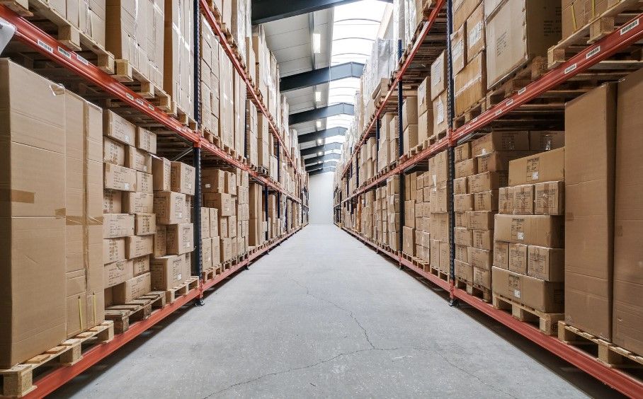 Langt og bredt lager med flere hylder og mange bokse med produkter. Lysskin over loftet.