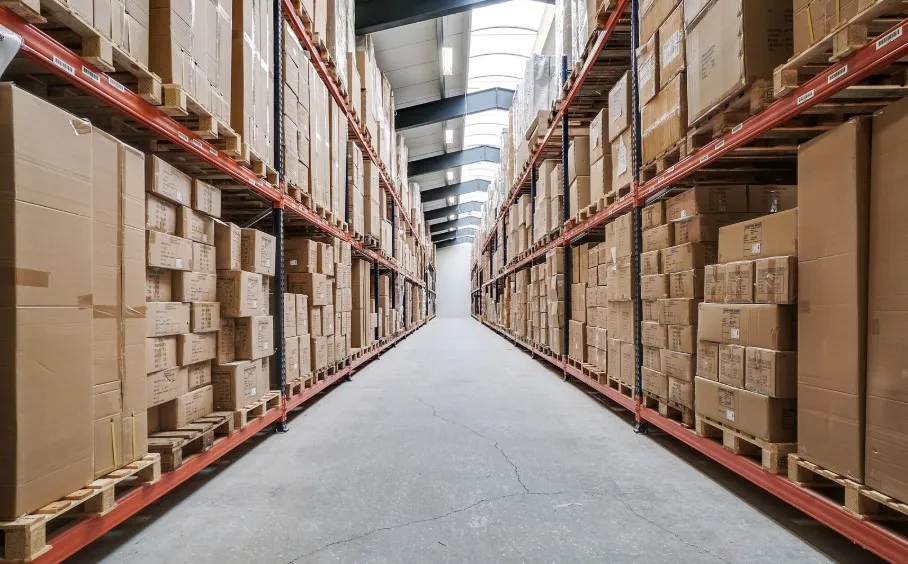 Langt og bredt lager med flere hylder og mange bokse med produkter. Lysskin over loftet.