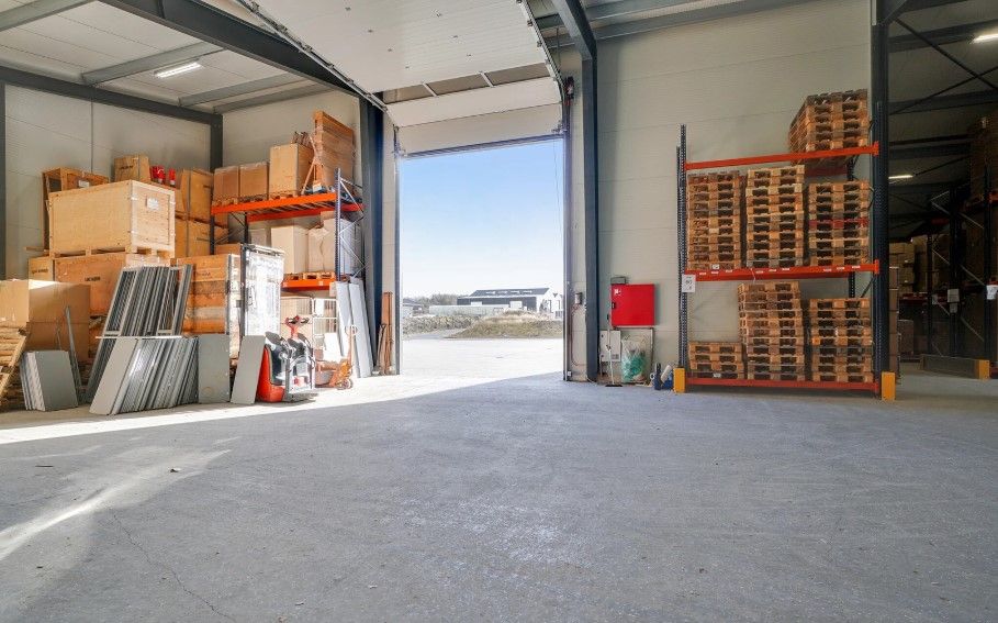 Lager med store mængder varer og pallehyller i en industriel bygning, som ser ud til at være forladt