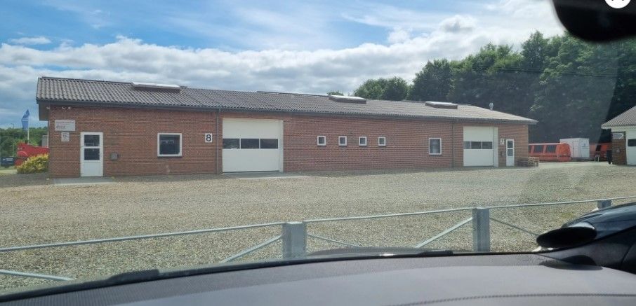 Et stort bygningskompleks med garagedøre og vinduer med solpaneler på taget, omgivet af en stenede parkeringsplads.