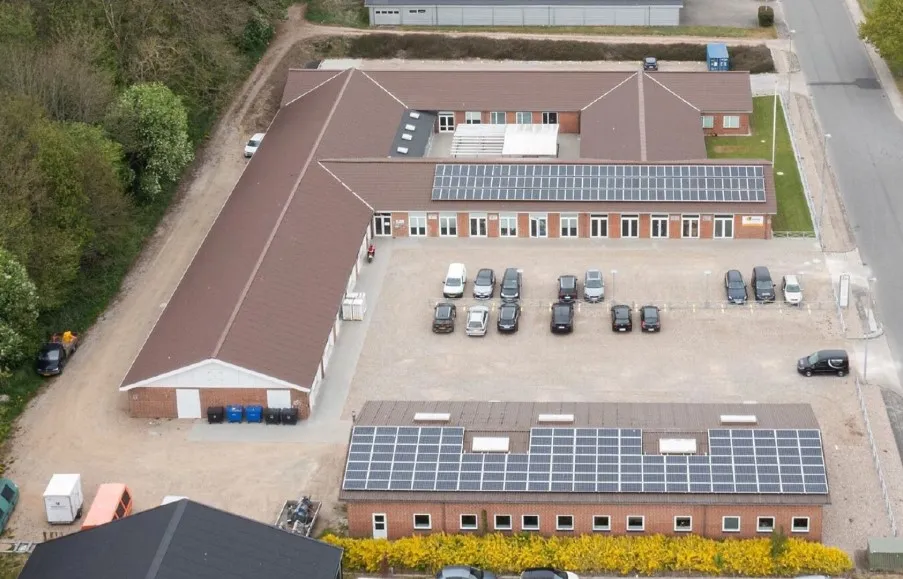 Firmabygning med solceller på taget og parkeringsplads med biler foran