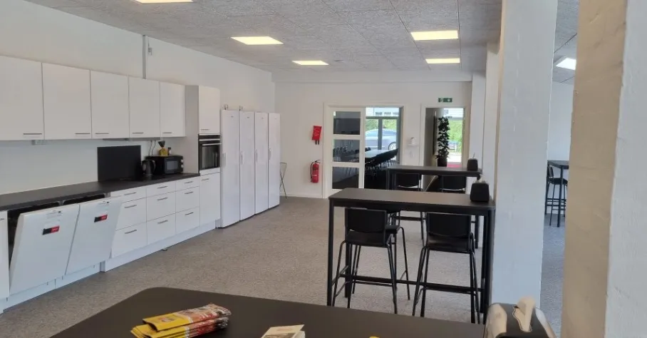 Lejlighed med køkken, bord og stole, lysekroner og et rødt ildslukker.