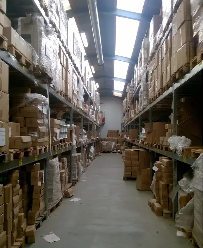 Langt ud i en stor industrihal, hvor der er masser af kartoner på hylder og på gulvet. Der er lys lige over midten af rummet
