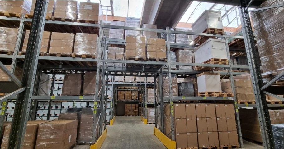 En stor lagerhal med flere metalhylder og mange pakket kasser i alle størrelser og farver