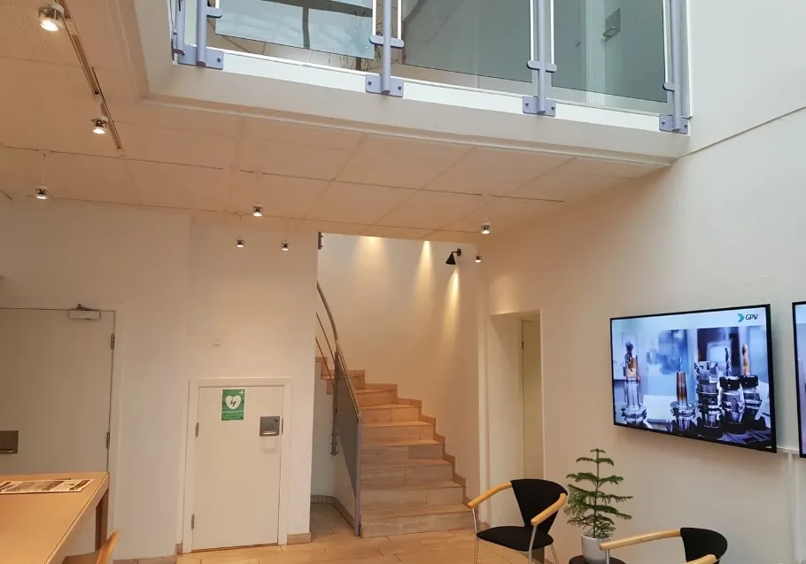 En stor lobby med møbler, et tv-skærm og et skab samt en trappe med et håndtag