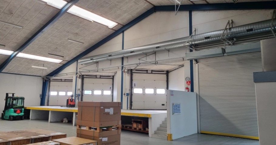 Lagerhallen med store garagedøre og opkørstelaug, hvor der er forskellige kasser og et forklæfterkøretøj.
