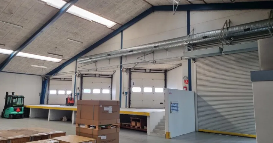 Lagerhallen med store garagedøre og opkørstelaug, hvor der er forskellige kasser og et forklæfterkøretøj.